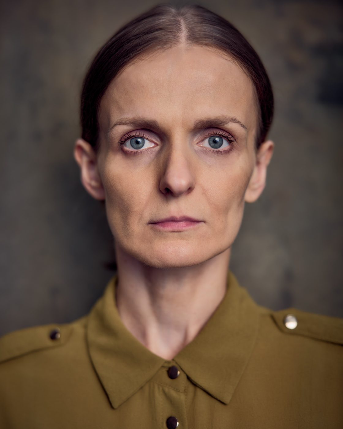 Monika Valkunaite headshot, olive shirt, hair slicked back